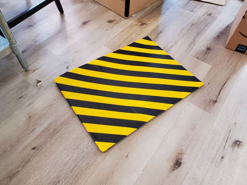 Ghost trap lid, cardboard covered with diagonal stripes of yellow and black duct tape. 